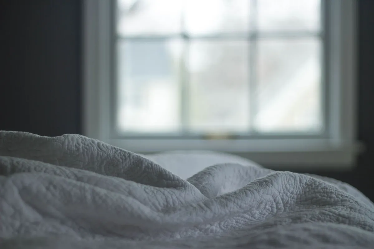 Cama con cobertor gris junto a una ventana